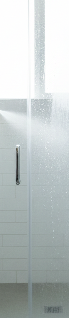 A person cleaning a glass shower door that is half-covered in hard water stains and half-crystal clear, demonstrating the cleaning process.