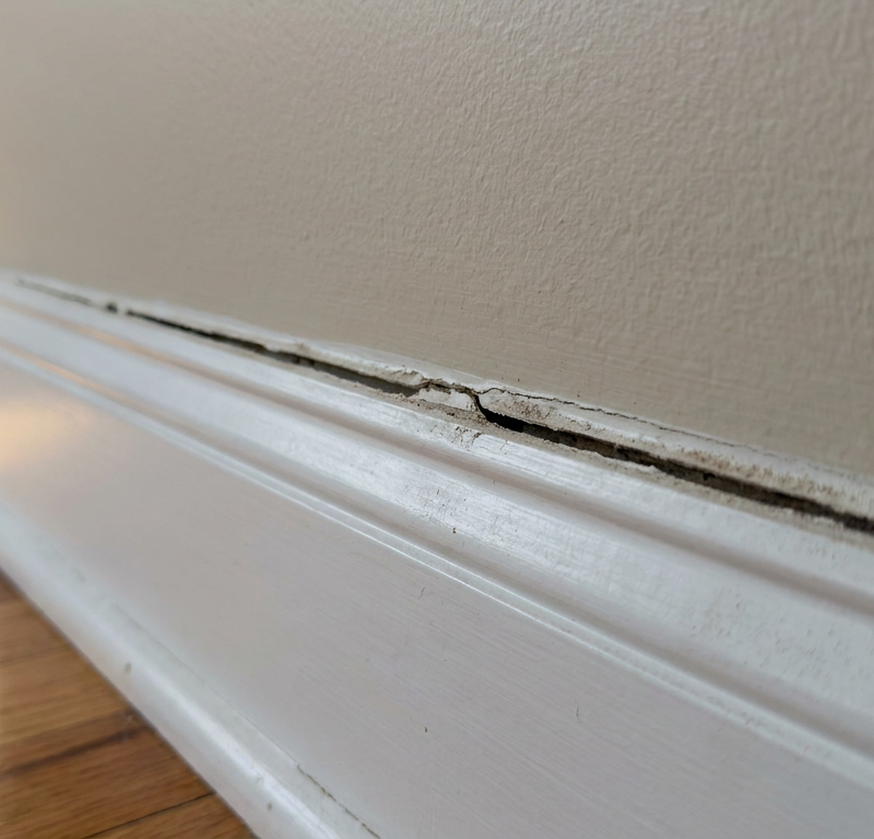 Baseboard trim pulling away from drywall leaving a dark visible gap along the wall