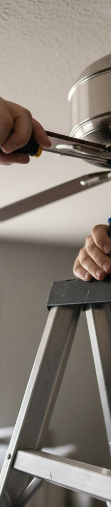Homeowner tightening a screw on a white ceiling fan blade arm to fix a wobble.
