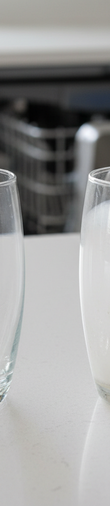 A clear, sparkling drinking glass next to a cloudy, hazy glass, illustrating the problem of dishwasher film.
