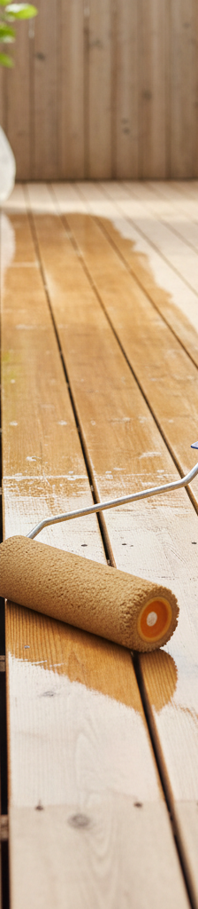 A person applying a protective clear sealant to a beautifully restored wood deck with a roller.