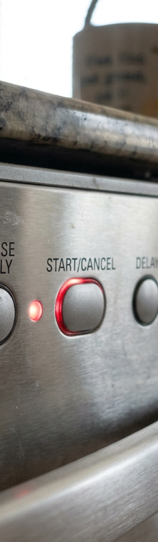 A close-up of a dishwasher control panel with a blinking start light, indicating an error code.