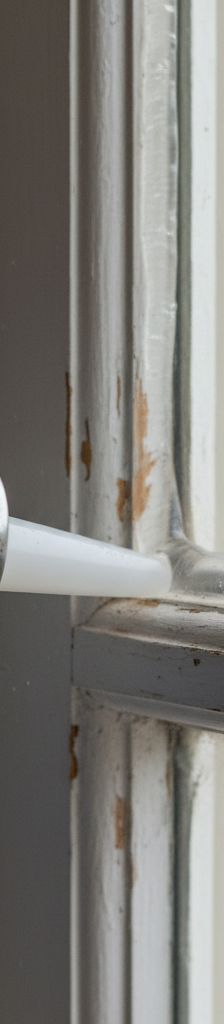 Homeowner applying caulk to seal a drafty window frame