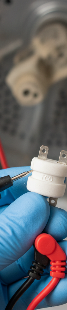 Hand testing a dryer thermal fuse with a multimeter, showing continuity test.