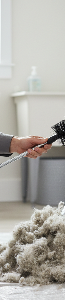 Homeowner cleaning a clogged dryer vent with a long brush, removing lint.