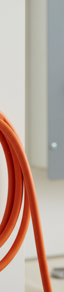Close-up of a heavy-duty orange extension cord plugged into a wall outlet, with a home electrical panel in the background.