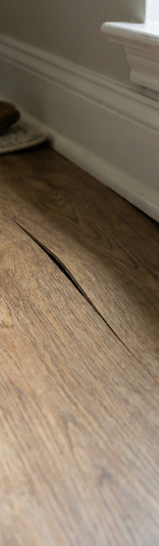 Close-up of luxury vinyl plank flooring deflecting downward near baseboard under pressure