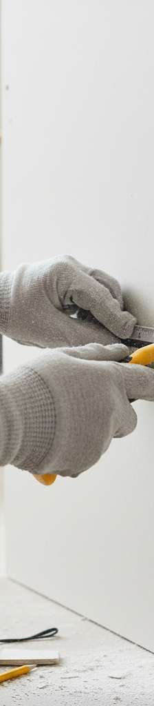 Homeowner carefully cutting a rectangular outline around a large drywall hole with a utility knife and ruler.