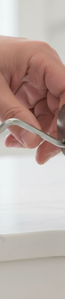 Homeowner using an Allen wrench to remove the handle set screw from a leaky single-handle kitchen faucet.