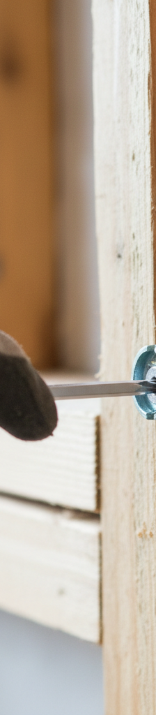 Hand securing a copper water pipe to a wooden joist with a metal pipe clamp and a screwdriver.