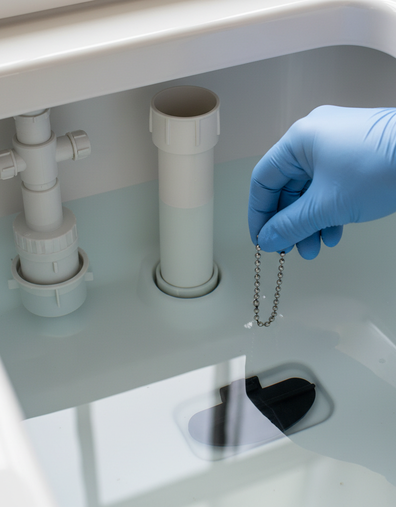 Hand adjusting a toilet flapper chain inside a clean toilet tank