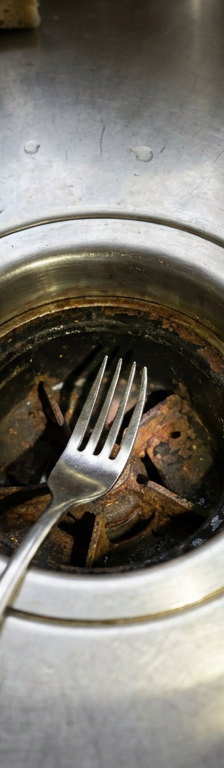 A metal fork stuck inside a garbage disposal, causing a grinding noise.