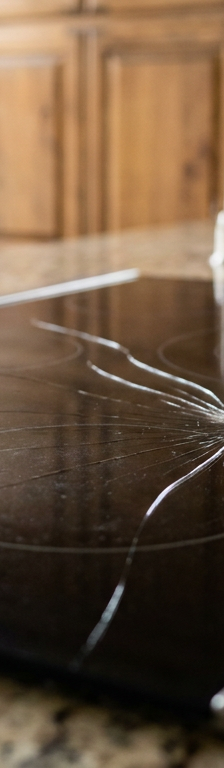 A cracked black glass cooktop with a large spiderweb fracture over a burner element.
