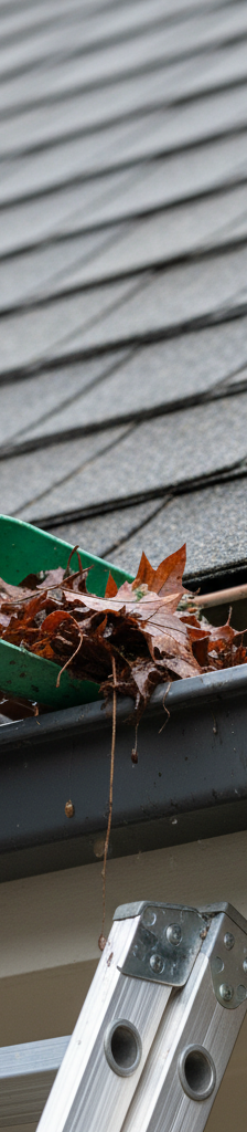 Homeowner carefully scooping wet leaves from a dark gutter with a tool, protecting roof.