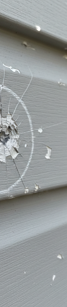 Close-up of vinyl siding showing clear starburst cracks and chips from hail, with a chalk mark highlighting damage.