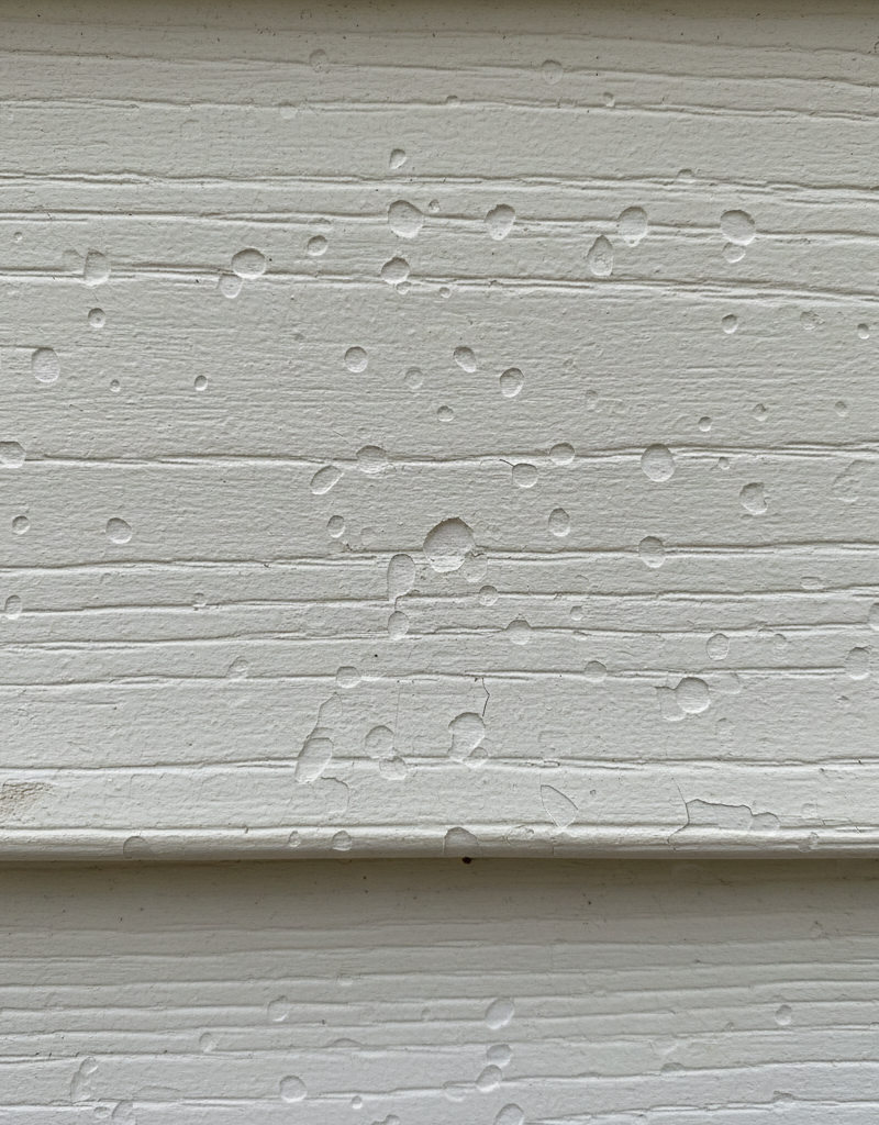 Close-up of vinyl siding with subtle hail damage, showing small impact marks and cracks.