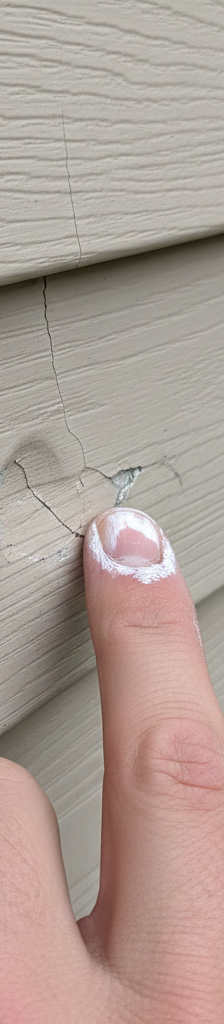 Close-up of hail-damaged vinyl siding with chalk marks on dents and cracks.