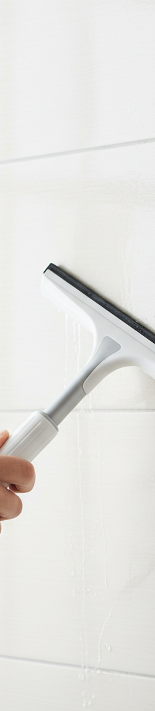 A hand using a squeegee to wipe down a clean, sparkling ceramic tile shower wall, with a small patch of dull soap scum visible on an adjacent uncleaned area.