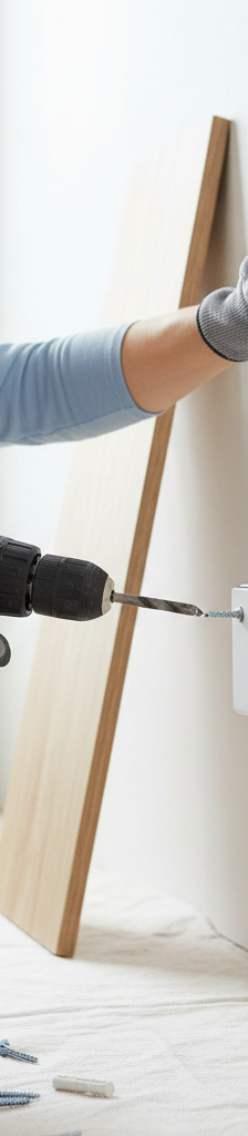 Homeowner installing a floating shelf into drywall, securing the bracket with a drill