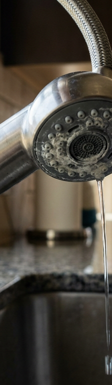 Pull down kitchen faucet spray head being unscrewed over a stainless sink to fix low water pressure