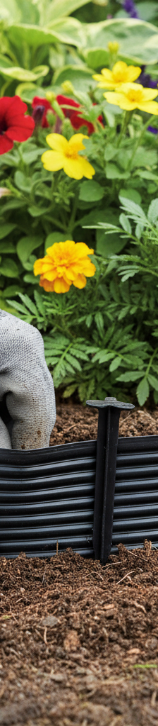 Homeowner installing black landscape edging around a flower bed, driving a spike into the ground.
