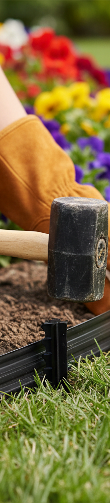 Homeowner fixing landscape edging by driving a securing stake into the ground next to a flower bed.