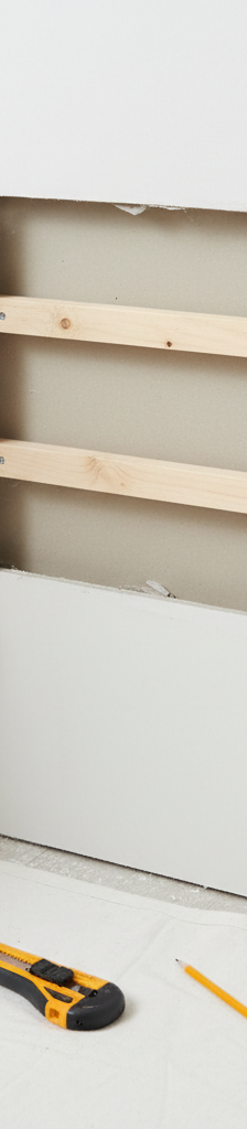 Hands installing a new drywall patch into a large hole supported by wood strips