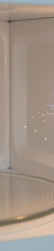 A microwave oven interior with a small, visible spark near the waveguide cover on the side wall, indicating an arcing issue.