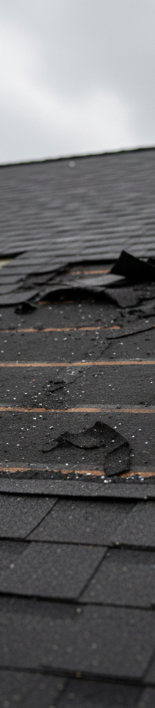 Missing asphalt shingles on a roof after a storm, exposing torn underlayment.