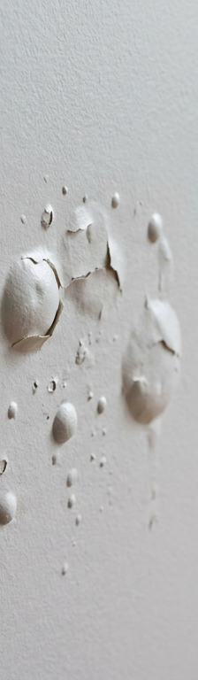A close-up of a gray painted wall with multiple paint bubbles and blisters, indicating an adhesion problem.