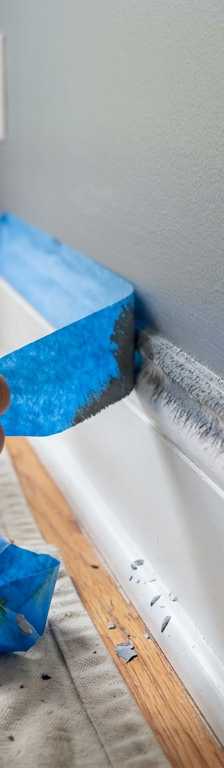A close-up of blue painter's tape being pulled off a wall, showing a fuzzy, bleeding paint line.