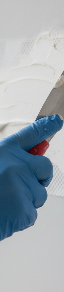Hand applying joint compound over a white fiberglass mesh patch on a light beige drywall wall.