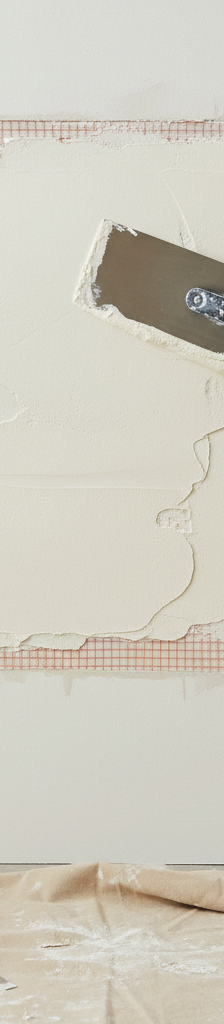 Homeowner applying joint compound with a drywall knife over a large drywall patch reinforced with mesh tape.