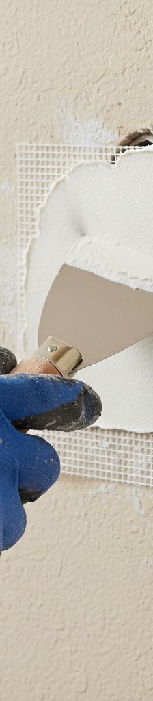 Hand applying joint compound over a small mesh drywall patch on a wall.