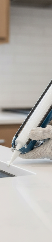Contractor applying silicone caulk with a caulk gun around a kitchen sink to countertop joint.