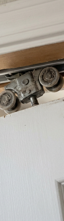 A white pocket door hanging crookedly off its track, with the dislodged roller mechanism visible.