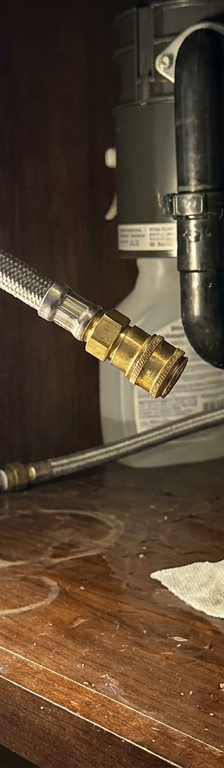 Flashlight illuminating a water leak from a braided pull-down kitchen faucet hose under a sink