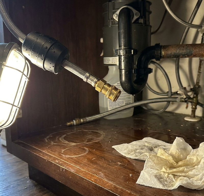 Flashlight illuminating a water leak from a braided pull-down kitchen faucet hose under a sink