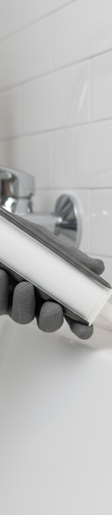 Person in gloves carefully applying a bead of fresh silicone caulk around a bathtub edge.
