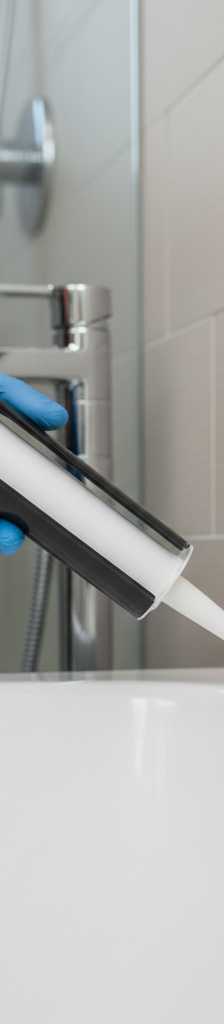 Hand applying a fresh bead of white caulk to a clean bathtub joint with a caulk gun.