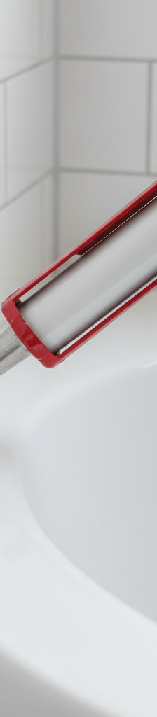 Applying a smooth, white caulk bead between a ceramic bathtub and tile wall with a caulk gun