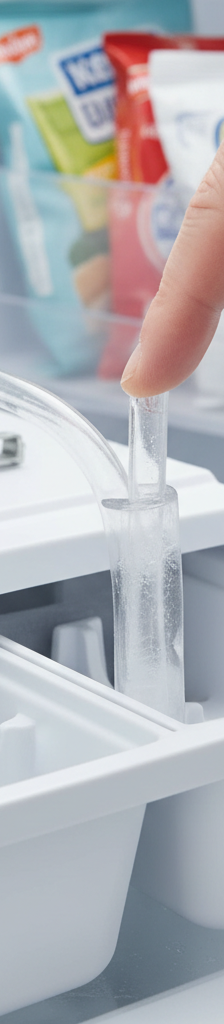 Homeowner inspecting and clearing a frozen water fill tube inside a refrigerator ice maker unit.