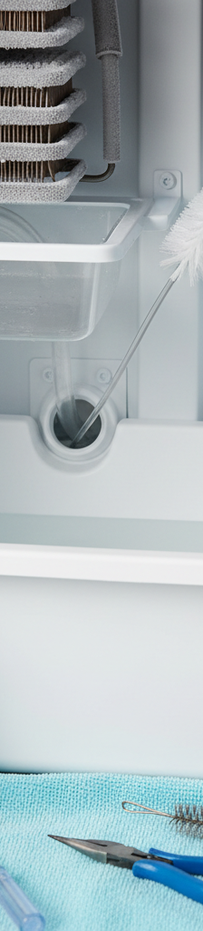 Homeowner using a flexible brush to clear a clogged defrost drain tube inside a freezer