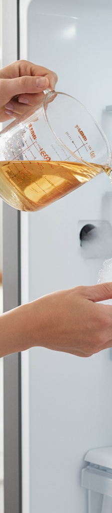 Homeowner pouring water into a refrigerator defrost drain to clear a clog