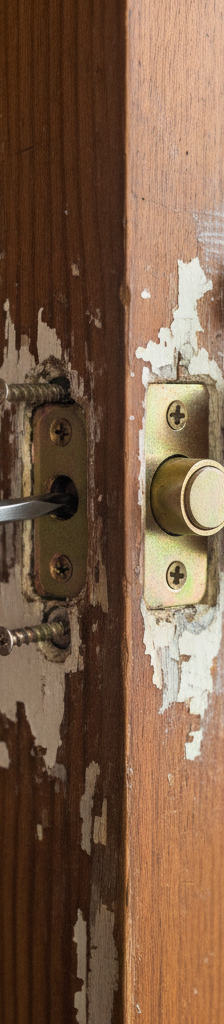 Hands unscrewing old deadbolt latch from door edge during replacement