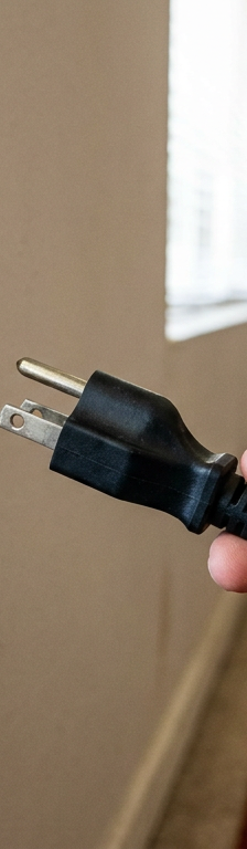 A homeowner holds a three-prong plug next to an old, incompatible two-prong wall outlet.