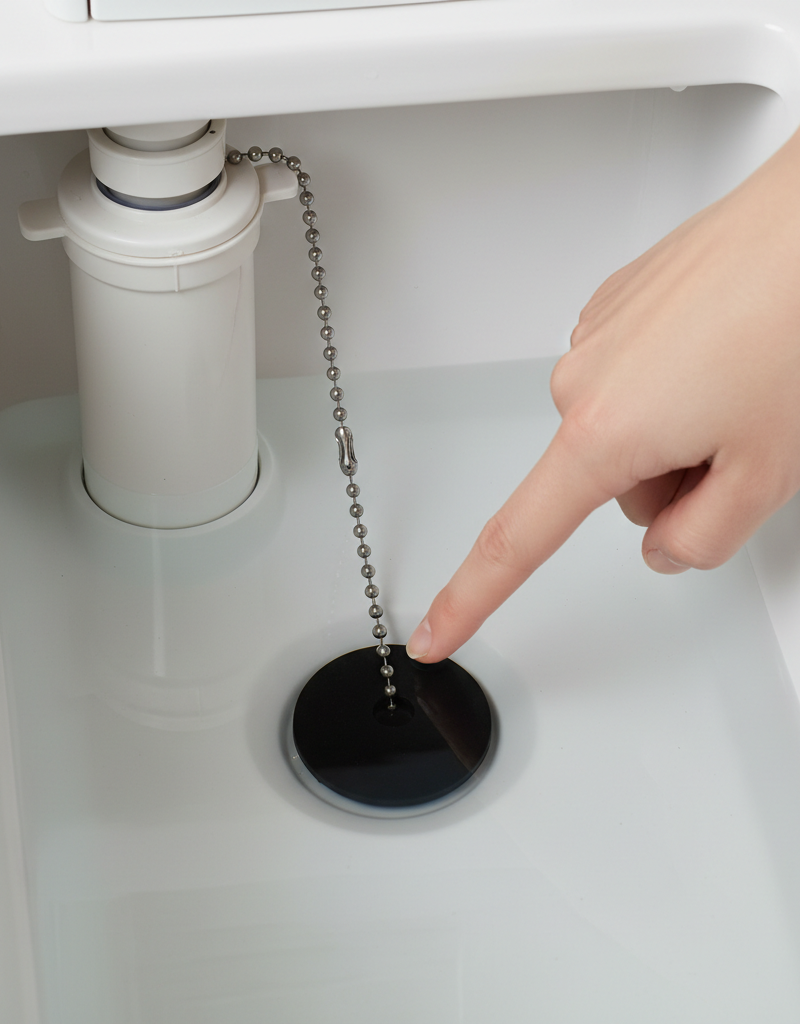 Hand pointing at a toilet flapper inside a toilet tank, demonstrating how to check for wear.