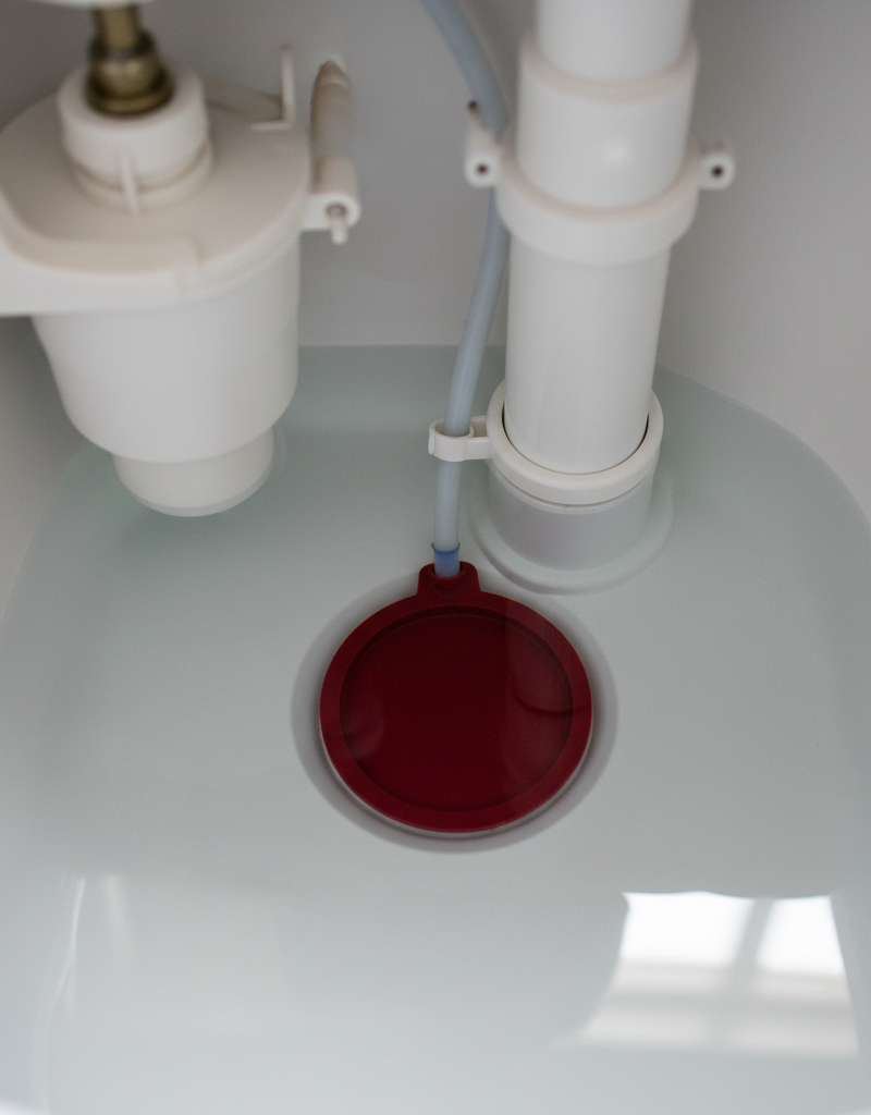 Inside a toilet tank showing a red flapper sealing the drain hole to fix a running toilet