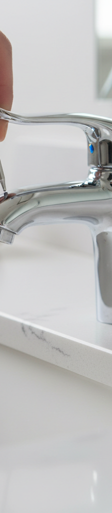A close-up shot showing a person using a hex key to tighten the set screw on a modern chrome bathroom faucet handle.
