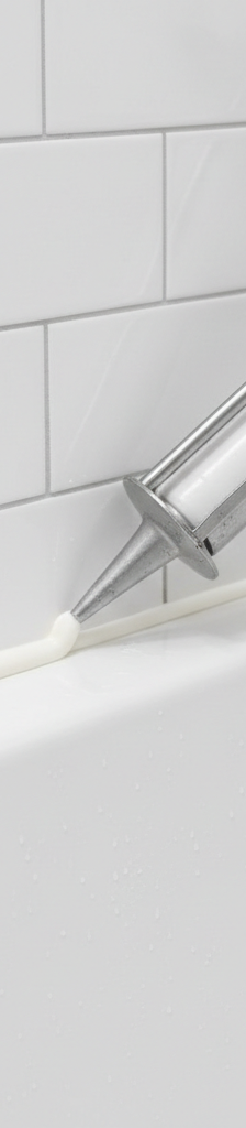 A pristine, white concave caulk bead at the seam between a bathtub and white subway tile.